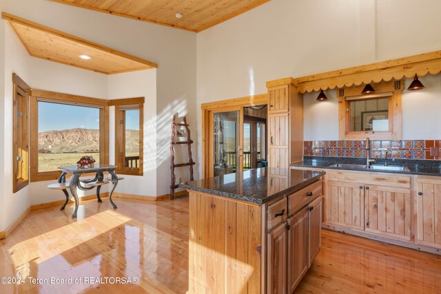 kitchen with wood ceiling, a kitchen island, dark stone counters, and light hardwood / wood-style floors