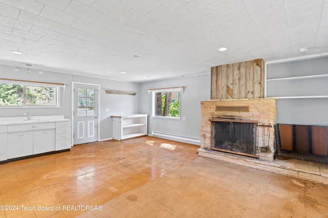 unfurnished living room featuring sink, light tile patterned floors, baseboard heating, and a stone fireplace