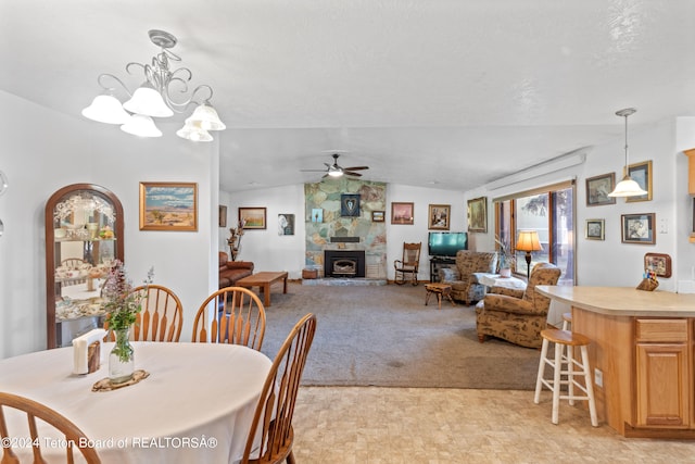 dining room with a stone fireplace, light carpet, lofted ceiling, and ceiling fan with notable chandelier