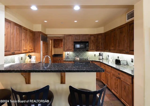 kitchen featuring sink, backsplash, dark stone countertops, and a kitchen bar