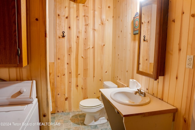 bathroom with wood walls, tile patterned flooring, vanity, washer / dryer, and toilet