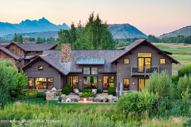 back house at dusk featuring a mountain view, a patio area, and a balcony