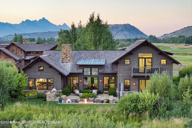 back of house at dusk featuring a mountain view, a patio, a chimney, and a balcony