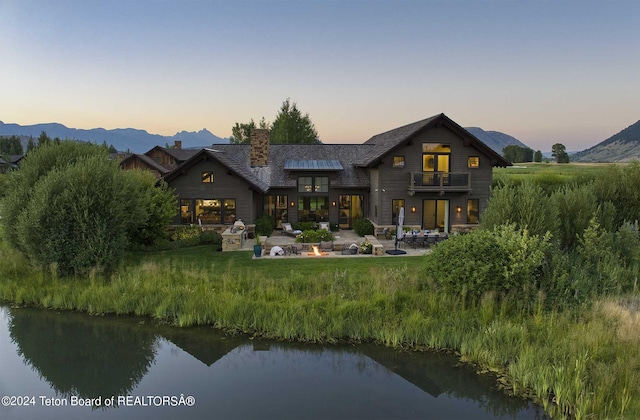 back of property featuring a chimney, a patio area, a balcony, and a water and mountain view