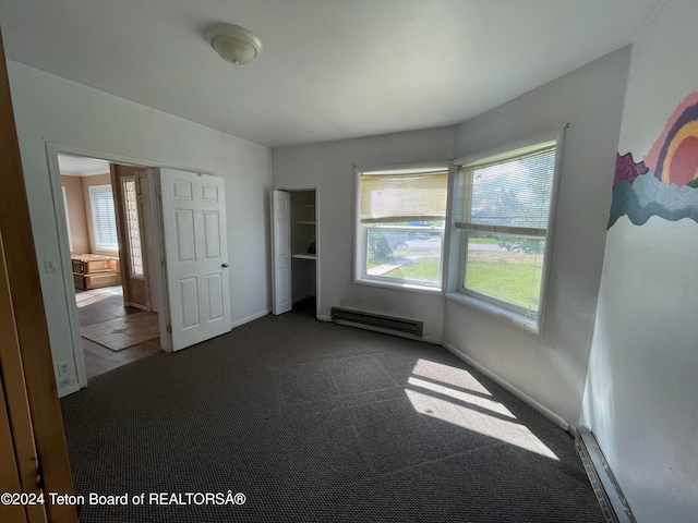 unfurnished bedroom featuring dark colored carpet and a baseboard heating unit