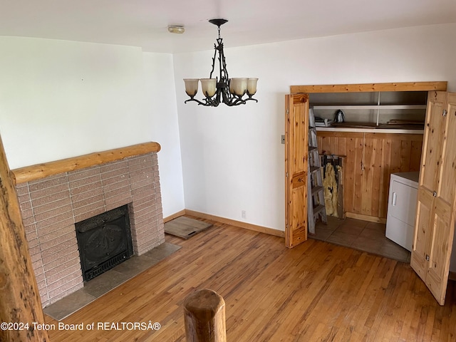 unfurnished dining area with a notable chandelier, washer / dryer, a fireplace, and light hardwood / wood-style floors