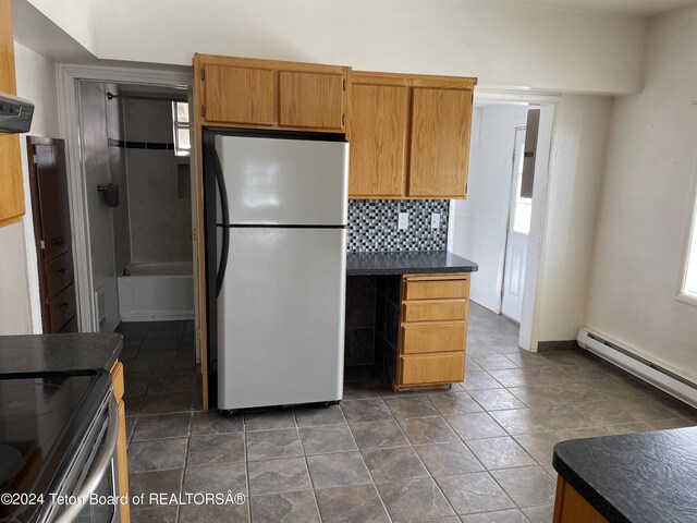 kitchen featuring tasteful backsplash, a baseboard heating unit, stainless steel fridge, and a healthy amount of sunlight