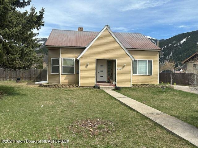 545 Adams St, Afton, WY 83110 - bungalow-style home featuring a front lawn, fence, a mountain view, metal roof, and a chimney