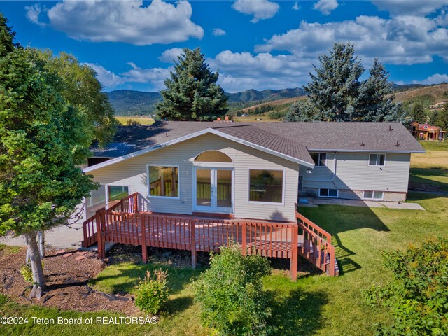 rear view of house featuring a deck with mountain view and a lawn