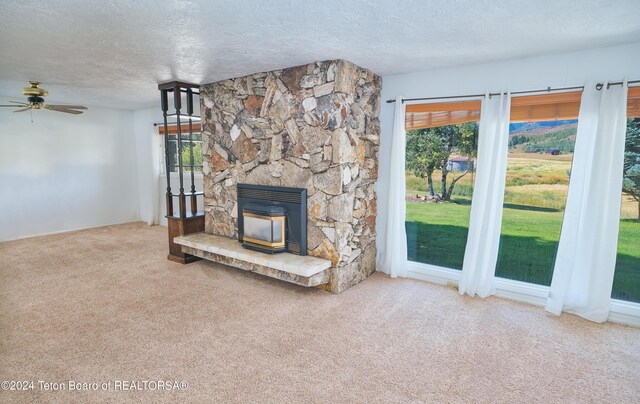 unfurnished living room featuring carpet flooring, plenty of natural light, ceiling fan, and a stone fireplace