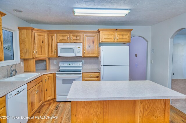 kitchen featuring light wood-type flooring, white appliances, a kitchen island, and sink