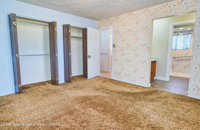 unfurnished bedroom featuring a textured ceiling, connected bathroom, hardwood / wood-style floors, and multiple closets