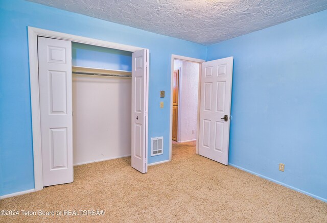 unfurnished bedroom with a closet, light carpet, and a textured ceiling