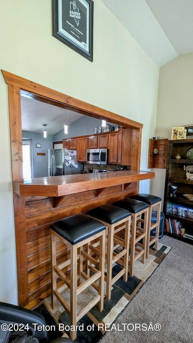 kitchen featuring appliances with stainless steel finishes, vaulted ceiling, kitchen peninsula, and carpet