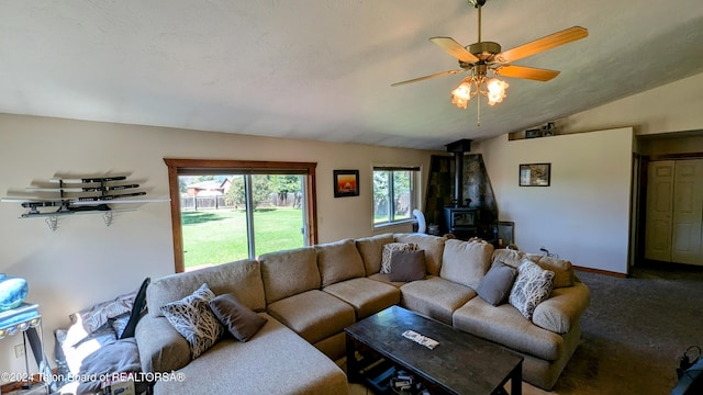 carpeted living room featuring ceiling fan, vaulted ceiling, and a wood stove