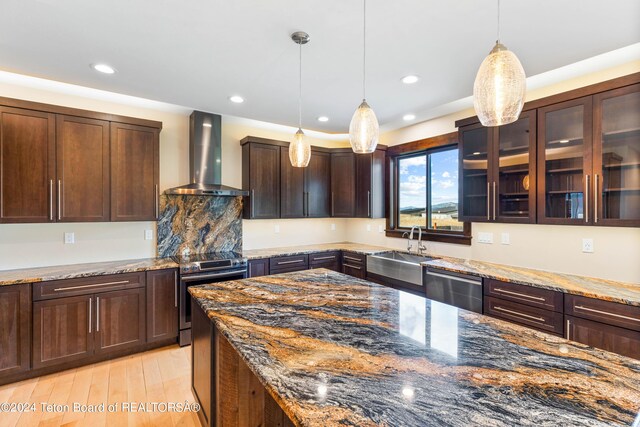 kitchen featuring dark stone countertops, stainless steel appliances, wall chimney range hood, pendant lighting, and a sink