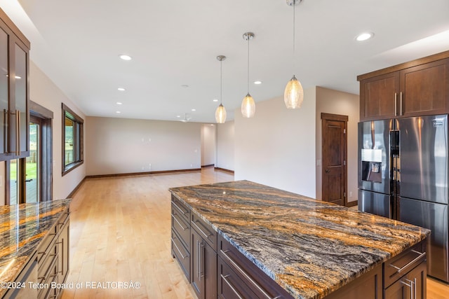 kitchen featuring stainless steel fridge with ice dispenser, light wood-style flooring, dark stone countertops, a center island, and recessed lighting