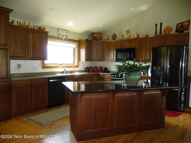 kitchen featuring lofted ceiling, a sink, a kitchen island, light wood-type flooring, and black appliances