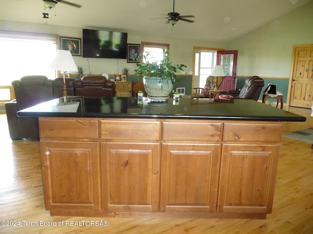 kitchen featuring dark countertops, open floor plan, ceiling fan, and an island with sink