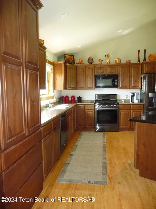 kitchen featuring black microwave, brown cabinetry, refrigerator with ice dispenser, a sink, and gas stove