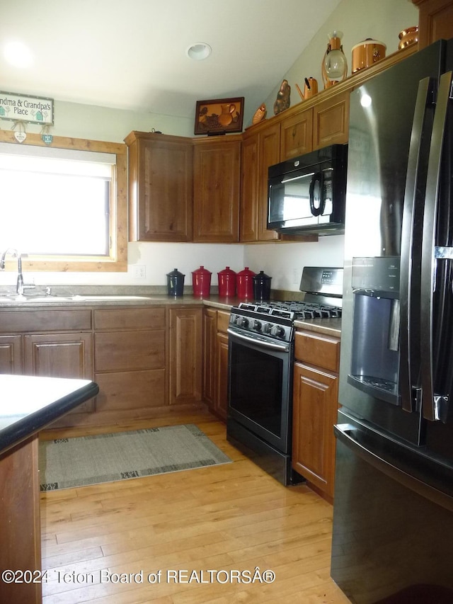 kitchen featuring range with gas cooktop, brown cabinetry, freestanding refrigerator, a sink, and black microwave