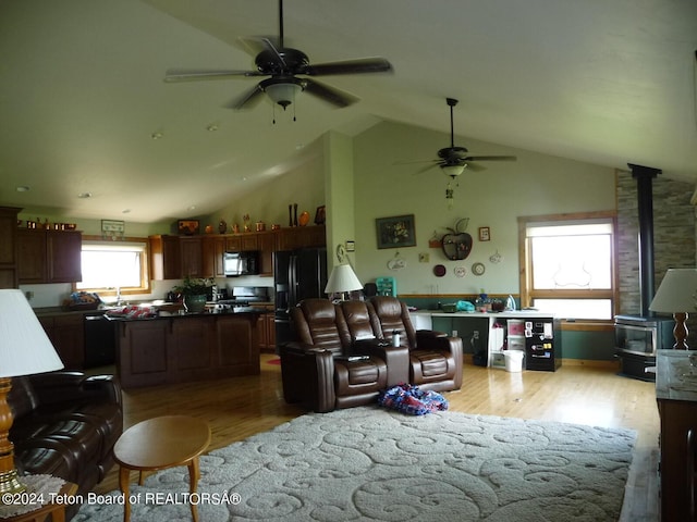 living area featuring a wood stove, light wood-style floors, ceiling fan, and vaulted ceiling