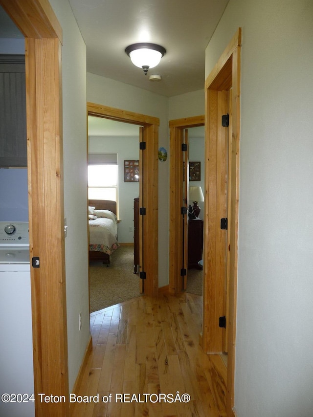 corridor featuring washer / clothes dryer, light wood-style flooring, and baseboards