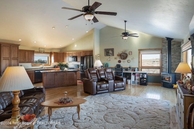 living area with high vaulted ceiling, a ceiling fan, a wood stove, and light wood-style floors