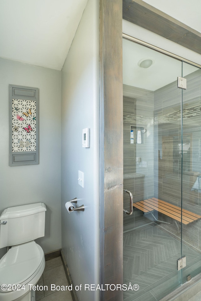 bathroom featuring toilet, a shower stall, baseboards, and tile patterned floors