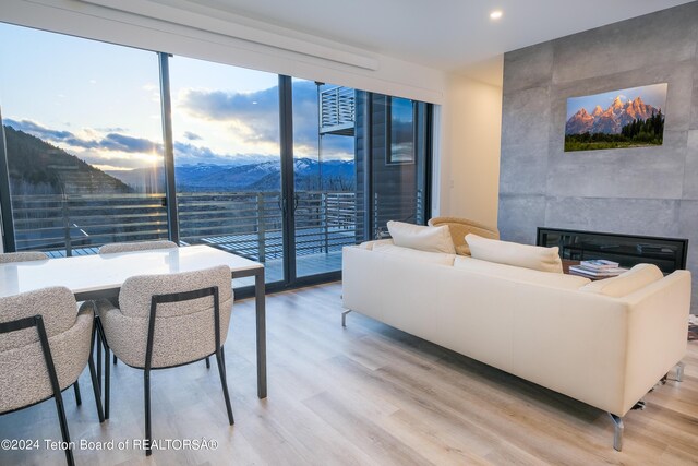 living area with a wall of windows, light wood finished floors, a tiled fireplace, a mountain view, and an accent wall