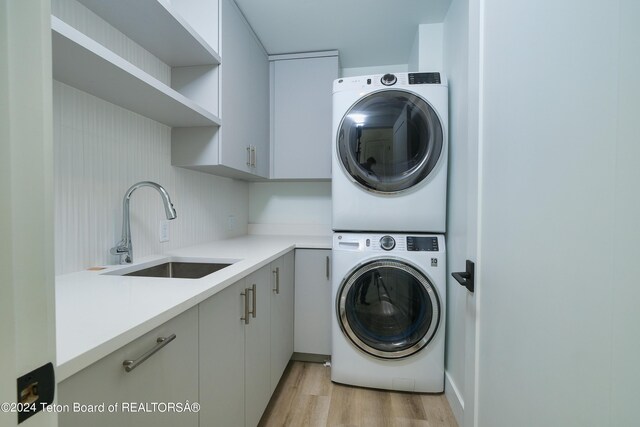clothes washing area with stacked washer and dryer, cabinet space, a sink, and light wood-style floors