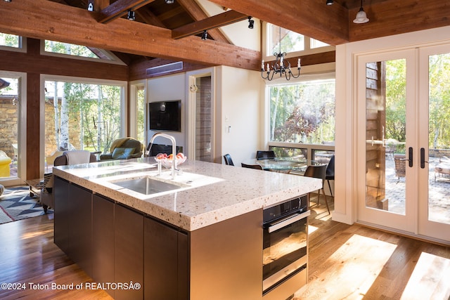 kitchen featuring sink, light hardwood / wood-style flooring, wall oven, a notable chandelier, and lofted ceiling with beams