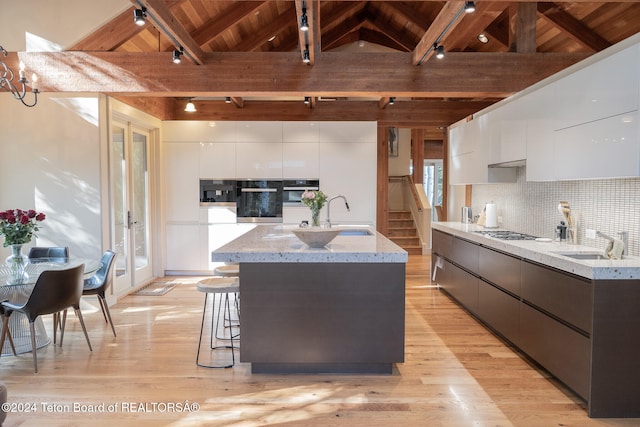 kitchen with white cabinetry, oven, a kitchen island with sink, and light wood-type flooring