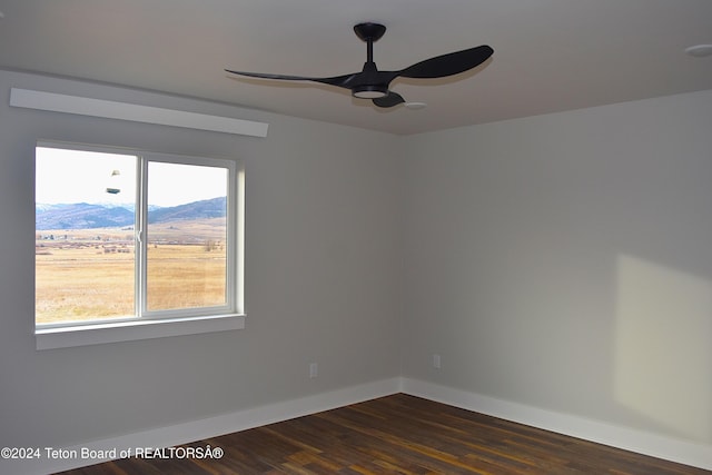 unfurnished room featuring a mountain view, dark hardwood / wood-style floors, and ceiling fan