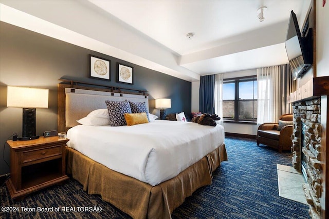 bedroom with dark carpet and a stone fireplace