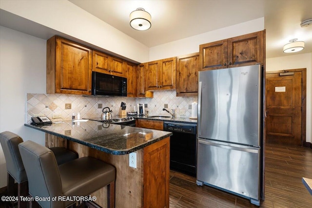 kitchen featuring tasteful backsplash, black appliances, dark hardwood / wood-style flooring, kitchen peninsula, and sink