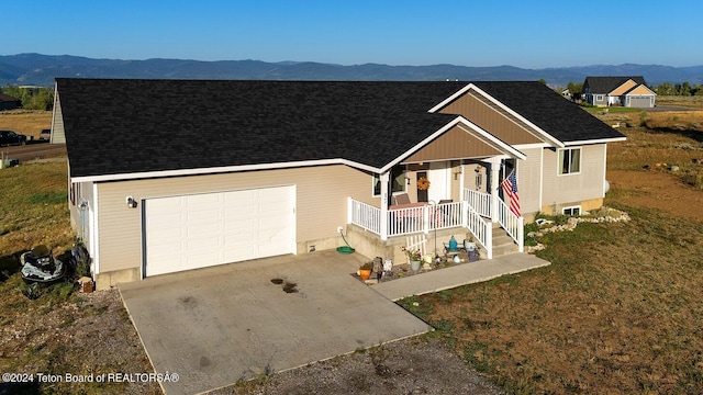 view of front of home with an attached garage, a mountain view, covered porch, driveway, and roof with shingles