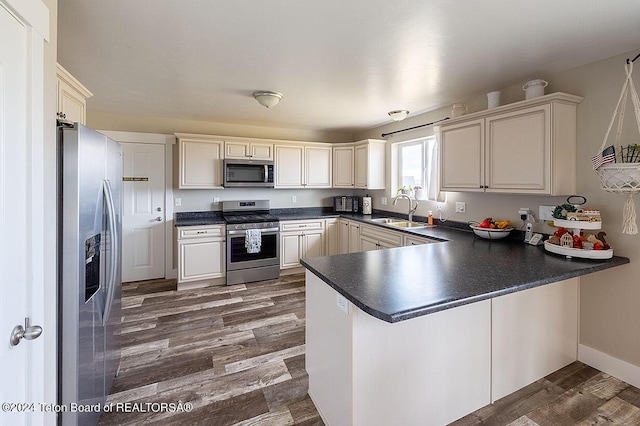 kitchen with a peninsula, a sink, appliances with stainless steel finishes, dark countertops, and dark wood finished floors