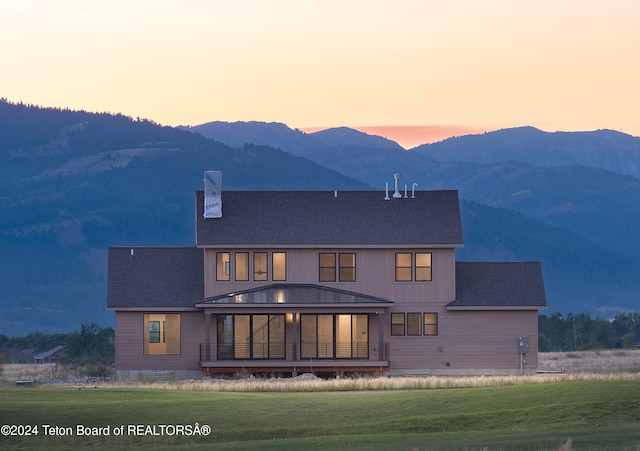 back house at dusk with a mountain view and a lawn