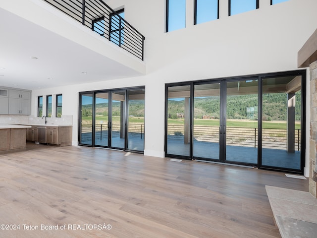 unfurnished living room featuring a towering ceiling, sink, and light wood-type flooring