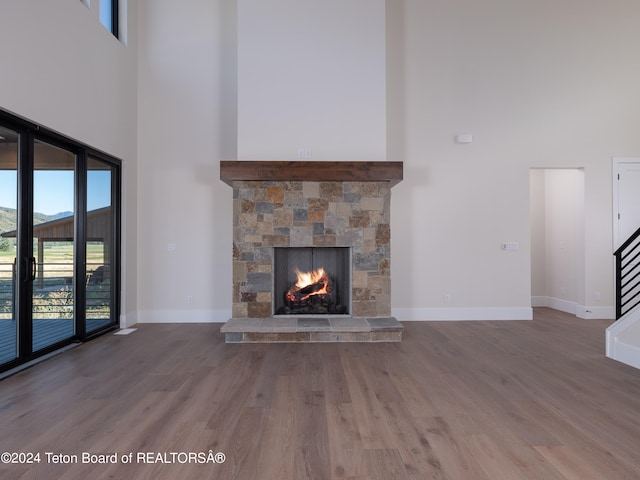 unfurnished living room featuring a stone fireplace, a towering ceiling, and wood-type flooring