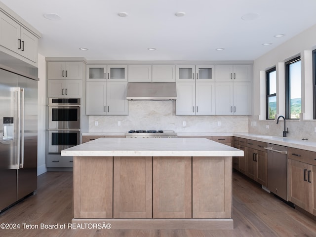 kitchen with wall chimney range hood, tasteful backsplash, appliances with stainless steel finishes, hardwood / wood-style flooring, and a center island