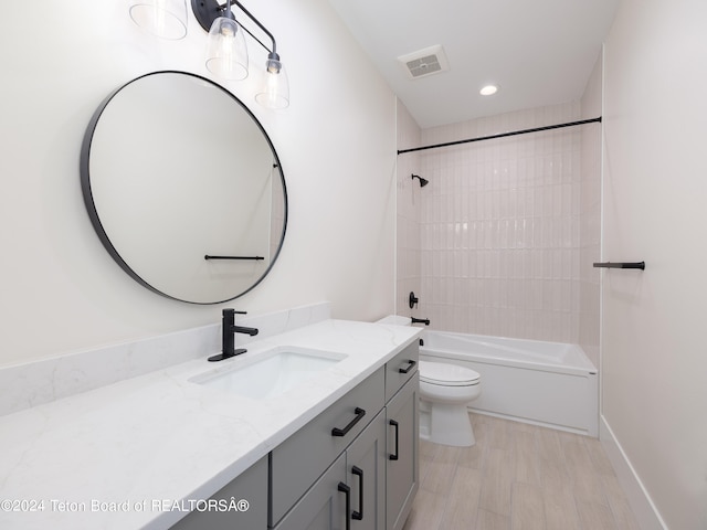 full bathroom with tiled shower / bath, vanity, wood-type flooring, and toilet