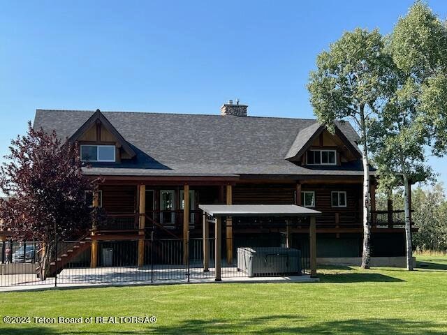 rear view of house with a hot tub and a lawn