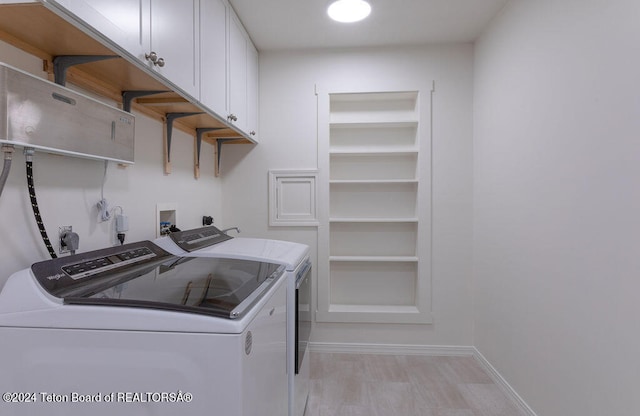 clothes washing area featuring washing machine and dryer, light wood-type flooring, and cabinets