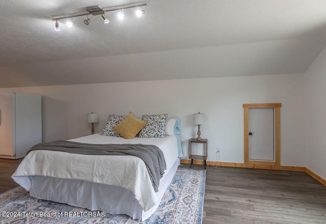 bedroom with a textured ceiling, lofted ceiling, hardwood / wood-style floors, and rail lighting