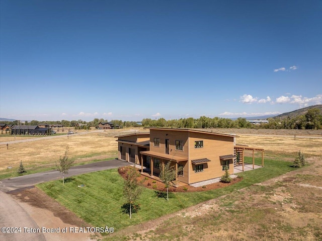 rear view of house featuring a mountain view, a rural view, and a lawn