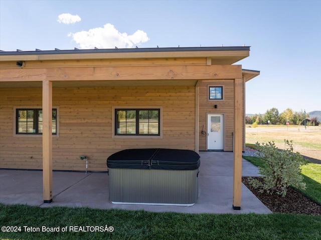 rear view of property with a hot tub and a patio