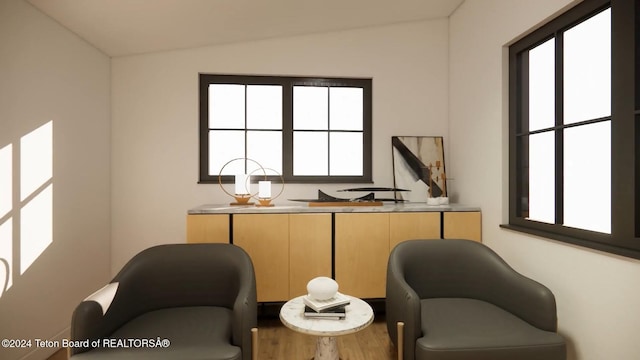 living area with a healthy amount of sunlight, lofted ceiling, and hardwood / wood-style flooring