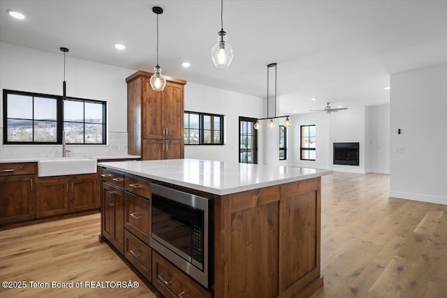 kitchen with sink, decorative light fixtures, light wood-type flooring, stainless steel microwave, and a kitchen island